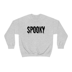 May include: A light gray sweatshirt with the word "SPOOKY" printed across the front in black, dripping letters. The sweatshirt has a crew neck and long sleeves. Perfect for Halloween or any spooky occasion.