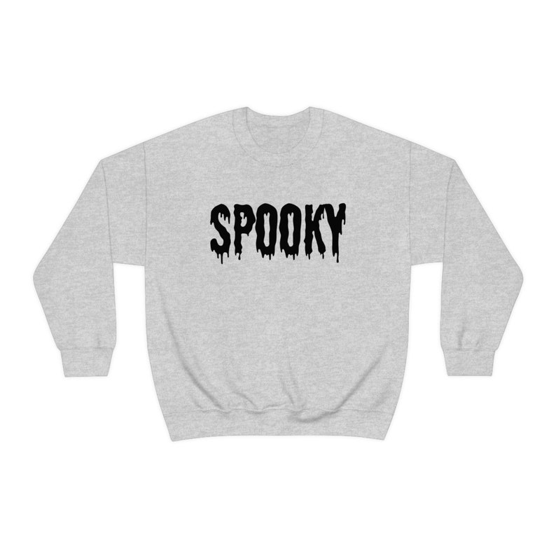 May include: A light gray sweatshirt with the word "SPOOKY" printed across the front in black, dripping letters. The sweatshirt has a crew neck and long sleeves. Perfect for Halloween or any spooky occasion.