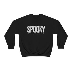 May include: Black sweatshirt with the word "SPOOKY" in dripping white letters across the chest. The sweatshirt has a crew neck and long sleeves, perfect for Halloween or spooky season.