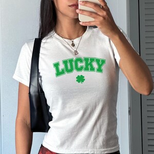 May include: White t-shirt with a green "LUCKY" graphic and a four-leaf clover.