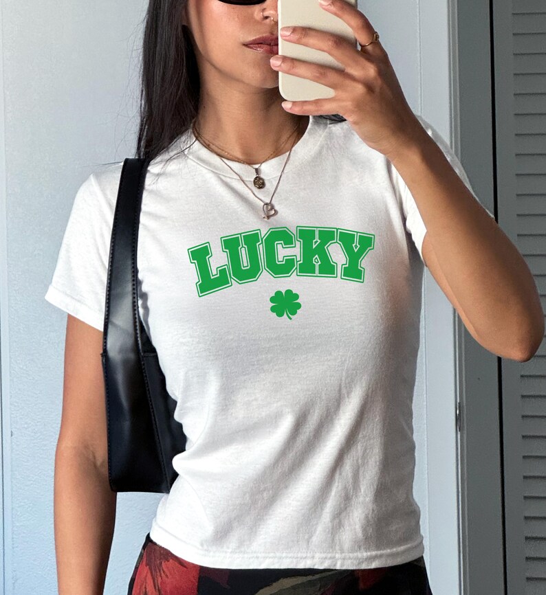 May include: White t-shirt with a green "LUCKY" graphic and a four-leaf clover.
