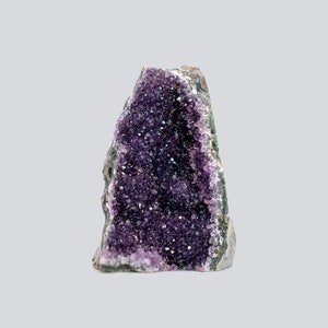 May include: A natural amethyst geode, showcasing a deep purple crystal interior. The geode's rough, gray exterior contrasts with the sparkling, crystalline structure within. The amethyst crystals are densely packed, creating a visually striking display.