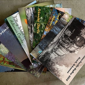 May include: A stack of brochures featuring scenic views of the Ozark Mountains in Arkansas. The brochures feature titles such as "Falling Water Trails", "Arkansas Ozarks", "Ozark Mountains", and "Union Pacific BigBoy 4014 Ozark, Arkansas".