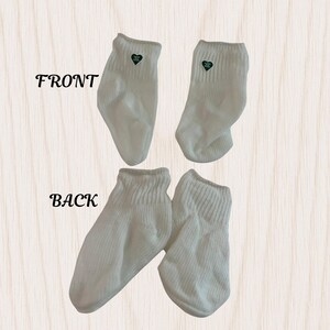 May include: Four white ankle socks, two showing the front and two showing the back. Each sock has a small green heart-shaped emblem near the top. The word "FRONT" and "BACK" are printed in black on the image.