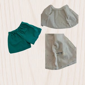 May include: A set of baby clothes, including a pair of emerald green shorts and a white jacket with a dotted pattern. The jacket is open, revealing the inside lining. The shorts have an elastic waistband.