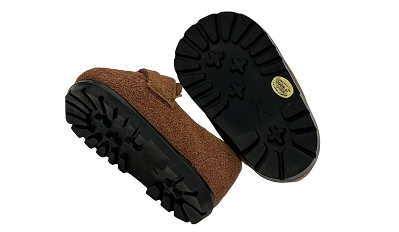 May include: Brown suede-like shoes with black lug soles. The shoes have a classic design with a textured upper and a sturdy, durable sole. The soles have a pattern for traction. The shoes are likely for children.