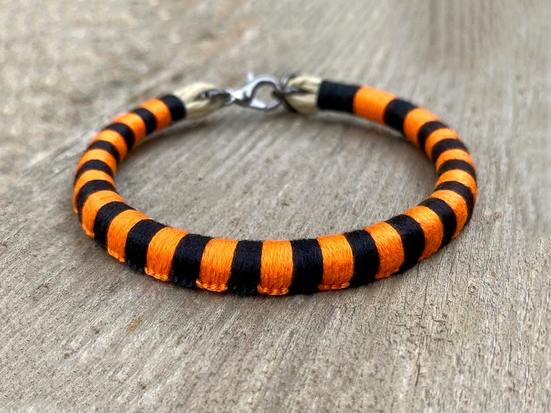 Peut inclure: Un bracelet ray&eacute; noir et orange avec un fermoir argent&eacute;.
