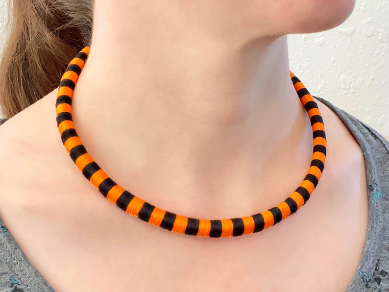 Puede incluir: Un collar gargantilla de tela a rayas negras y naranjas.