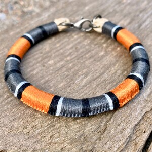 May include: A black, white, and orange braided bracelet with a silver clasp.