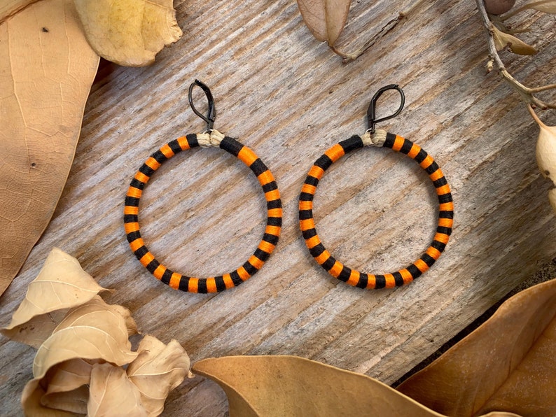 Peut inclure: Une paire de boucles d'oreilles cr&eacute;oles ray&eacute;es orange et noires. Les boucles d'oreilles sont en tissu et ont un design simple et moderne.