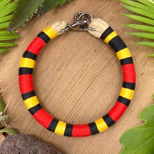 Könnte beinhalten: Ein rot-gelb-schwarzes gestreiftes Hundehalsband mit einem silbernen Verschluss.