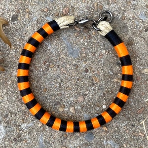 Peut inclure: Un collier de chien en corde ray&eacute; noir et orange avec une boucle argent&eacute;e.