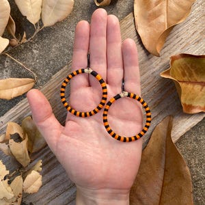Peut inclure: Une paire de boucles d'oreilles cr&eacute;oles ray&eacute;es orange et noires. Les boucles d'oreilles sont faites d'un mat&eacute;riau tiss&eacute; et ont un design simple et moderne.