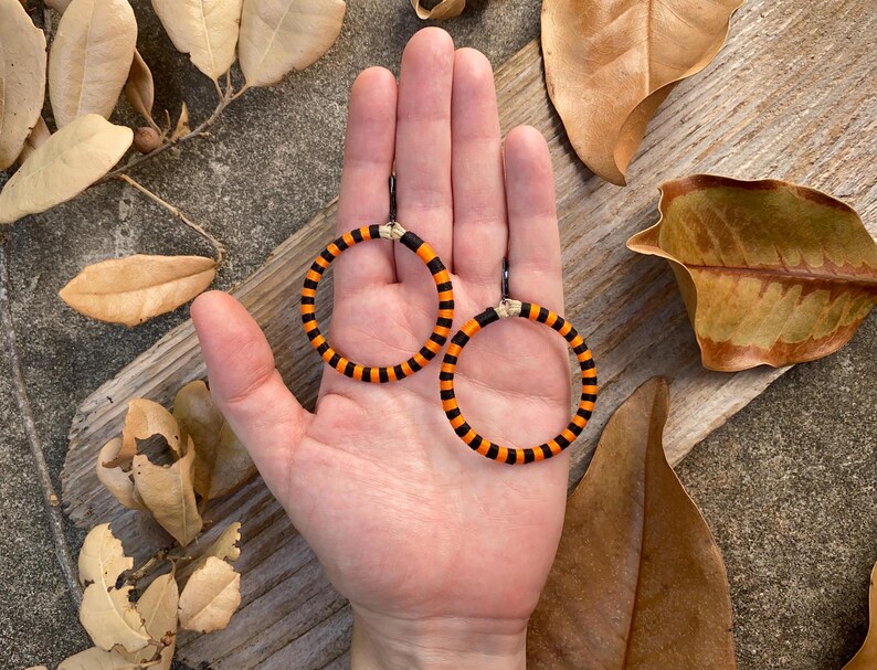 Peut inclure: Une paire de boucles d'oreilles cr&eacute;oles ray&eacute;es orange et noires. Les boucles d'oreilles sont faites d'un mat&eacute;riau tiss&eacute; et ont un design simple et moderne.