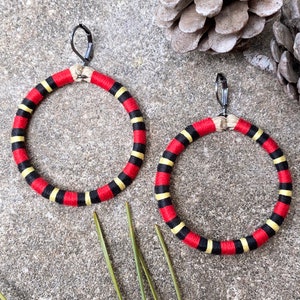 May include: A pair of large hoop earrings with a red, black, and yellow striped design. The earrings are made of fabric and have a silver hook closure.