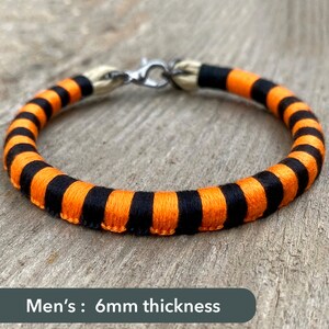 Peut inclure: Bracelet ray&eacute; noir et orange avec un fermoir argent&eacute;. Le bracelet mesure 6 mm d'&eacute;paisseur.