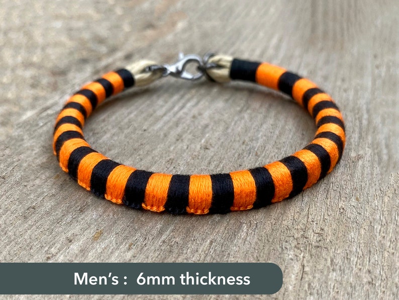 Peut inclure: Bracelet ray&eacute; noir et orange avec un fermoir argent&eacute;. Le bracelet mesure 6 mm d'&eacute;paisseur.