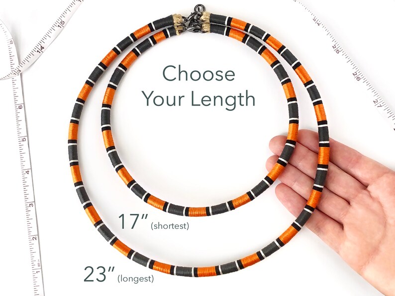 Puede incluir: Dos collares de rayas naranja y negras con cierres plateados. Los collares est&aacute;n dispuestos sobre una superficie blanca con una cinta m&eacute;trica. El texto "Choose Your Length" est&aacute; escrito en negro. Los collares miden 17 pulgadas (el m&aacute;s corto) y 23 pulgadas (el m&aacute;s largo).