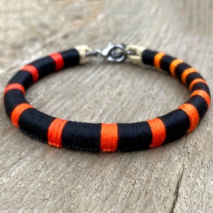 May include: A black and orange striped bracelet with a silver clasp.