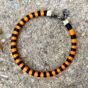 Peut inclure: Un collier en corde ray&eacute; noir et orange avec une boucle en m&eacute;tal argent&eacute;.