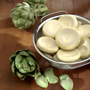 Könnte beinhalten: Ein Metallsieb gefüllt mit Artischockenherzen, mit ganzen Artischocken auf einer Holzoberfläche.