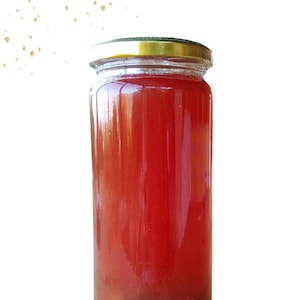 Peut inclure: Un bocal en verre rempli d'un liquide rouge et un petit cône de pin brun au fond.