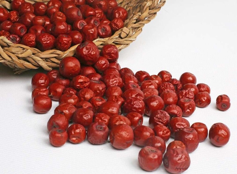 Puede incluir: Una cesta de mimbre rebosante de jujubes secas de color rojo brillante, tambi&eacute;n conocidas como d&aacute;tiles chinos, que se derraman sobre una superficie blanca.