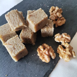 Puede incluir: Primer plano de una bandeja de servir de pizarra negra con varios cuadrados de fudge de nuez marr&oacute;n claro y nueces enteras.