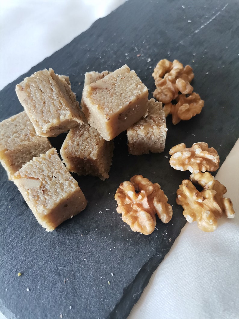 Puede incluir: Primer plano de una bandeja de servir de pizarra negra con varios cuadrados de fudge de nuez marr&oacute;n claro y nueces enteras.