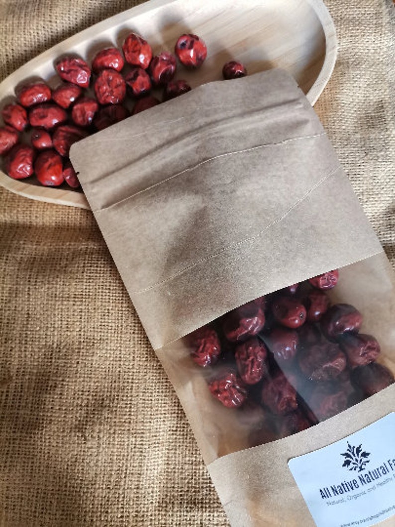 Puede incluir: Una bolsa de papel marr&oacute;n con una ventana de pl&aacute;stico transparente llena de d&aacute;tiles rojos secos. La bolsa tiene una etiqueta blanca con el texto "All Native Natural Foods" y un peque&ntilde;o logotipo de una planta.