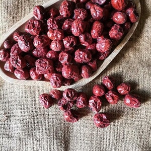 Puede incluir: Un cuenco de madera lleno de d&aacute;tiles rojos secos, con d&aacute;tiles adicionales esparcidos sobre una superficie de arpillera.