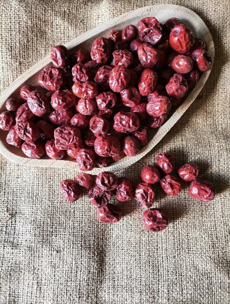 Puede incluir: Un cuenco de madera lleno de d&aacute;tiles rojos secos, con d&aacute;tiles adicionales esparcidos sobre una superficie de arpillera.