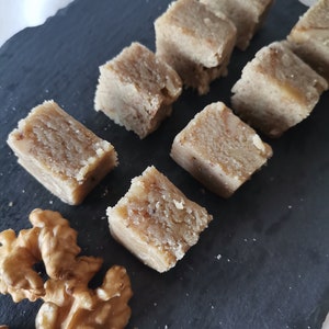 Puede incluir: Primer plano de una bandeja de servir de pizarra negra con ocho cuadrados de fudge de nuez marr&oacute;n claro y dos mitades de nuez.