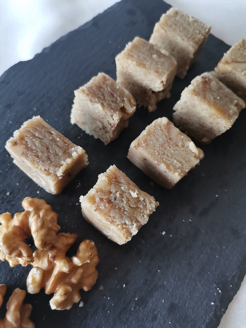 Puede incluir: Primer plano de una bandeja de servir de pizarra negra con ocho cuadrados de fudge de nuez marr&oacute;n claro y dos mitades de nuez.