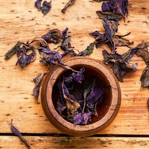 May include: A wooden bowl filled with dried purple herbs on a wooden surface.