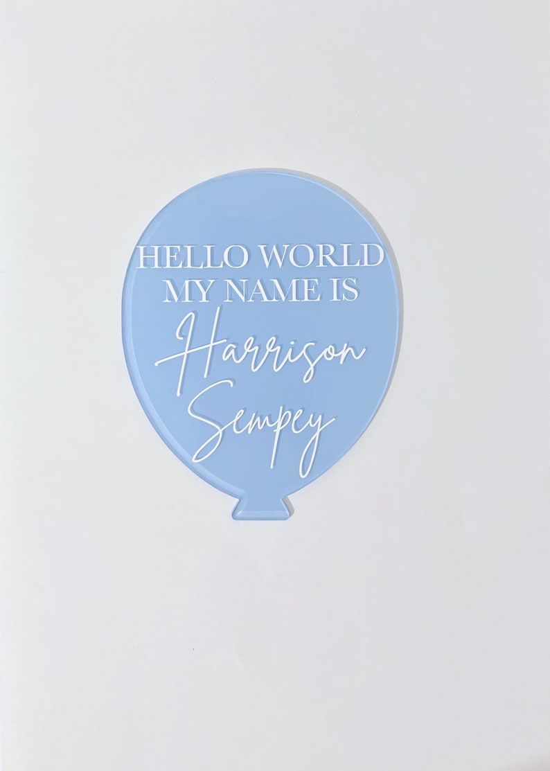 May include: A light blue balloon-shaped acrylic sign with the text "Hello World My Name Is Harrison Sempey" in white.