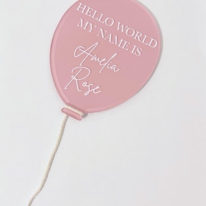 May include: Pink balloon with a white string, the balloon has the text "Hello World My Name Is Amelia Rose" written on it.