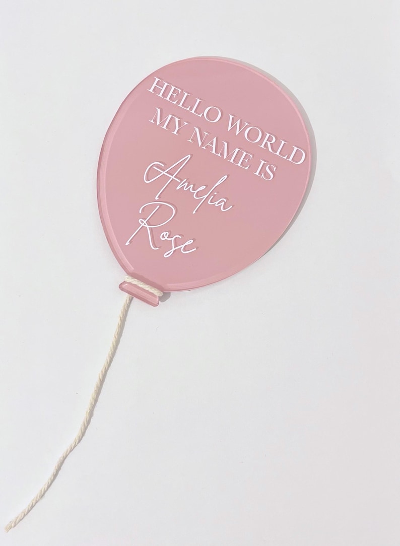 May include: Pink balloon with a white string, the balloon has the text "Hello World My Name Is Amelia Rose" written on it.