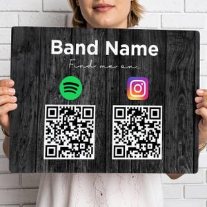 May include: A black wooden sign displaying the text "Band Name" in white script, with "Find me on..." below. The sign includes the Spotify and Instagram logos, each accompanied by a QR code for easy access to the band's profiles.