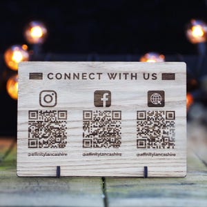 May include: Wooden sign with the text "Connect with us" and three QR codes. The QR codes are for Instagram, Facebook, and the web. The text below each QR code is the social media handle "@affinitylancashire".