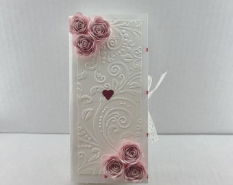 May include: A white card with a pink and white floral design and a red heart. The card is tied with a white ribbon.