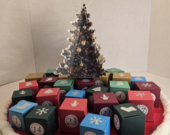 Könnte beinhalten: Ein Adventskalender mit 24 nummerierten Boxen in verschiedenen Farben, angeordnet um einen dekorativen Baum. Jede Box ist mit festlichen Bildern wie Schneeflocken und Weihnachtsbäumen verziert, auf einer roten Basis mit weißem Rand.