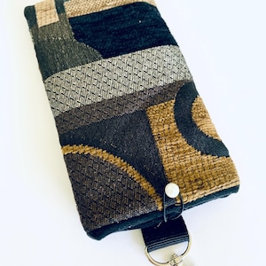 Puede incluir: Una funda para teléfono de tela con estampado negro y marrón con una correa negra y un clip plateado.