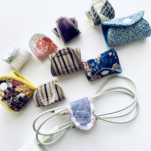 Puede incluir: Surtido de organizadores de cables de tela de colores vivos con varios patrones, incluyendo diseños florales, a rayas y geométricos. Los organizadores se utilizan para mantener los cables y los cables ordenados.