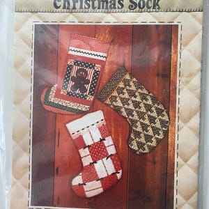 May include: A Patch Press Christmas Sock sewing pattern package, No. 329B, featuring three quilted stocking designs. The cover displays a red and white gingerbread man stocking, a black and tan tree print stocking, and a red and white checkered stocking.