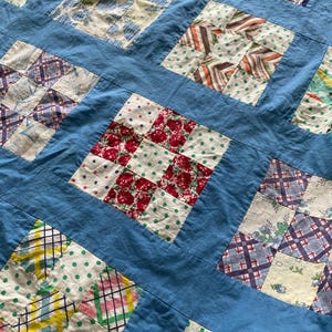 May include: A patchwork quilt featuring a grid of square blocks separated by solid light blue fabric strips. The blocks contain various patterns including red floral prints, green polka dots, and multi-colored plaid designs in cotton fabric.