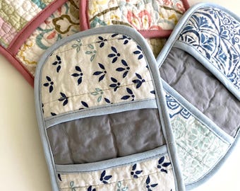 Könnte beinhalten: Drei gesteppte Ofenhandschuhe mit Taschen-Design. Ein Handschuh zeigt weißen Stoff mit kleinen dunkelblauen Blattmustern und einem grauen Mittelteil. Ein weiterer hat ein blau-weißes Blumenmuster. Der dritte hat einen rosa Rand und Blumenprint.