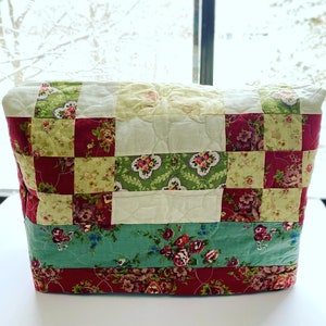 Puede incluir: Una funda de tela acolchada con un diseño de patchwork en tonos rojos, verdes y blancos. La funda presenta patrones florales y es perfecta para proteger y decorar un electrodoméstico de cocina.