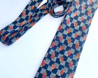 May include: A blue silk tie with a checkered pattern featuring a repeating crest design in red, yellow, and white.