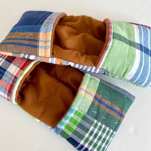 Op de afbeelding: Twee rechthoekige, gewatteerde stoffen oogkussens. De buitenkant heeft een patchwork-ontwerp van blauwe, groene, rode en witte ruit- en streepmotieven. De binnenkant is effen bruin.